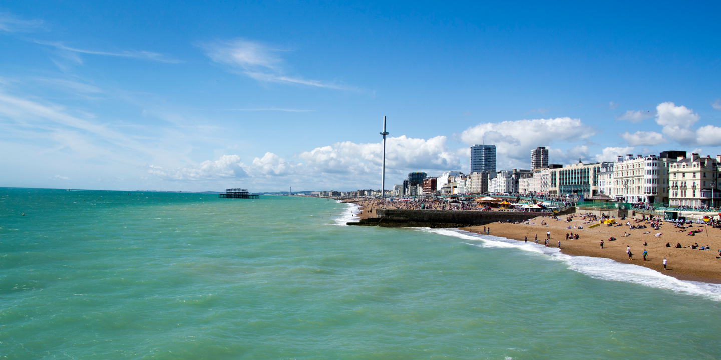 A sunny, West-facing view of Brighton beach featuring the British Airways i360, West pier, and several beach front properties.