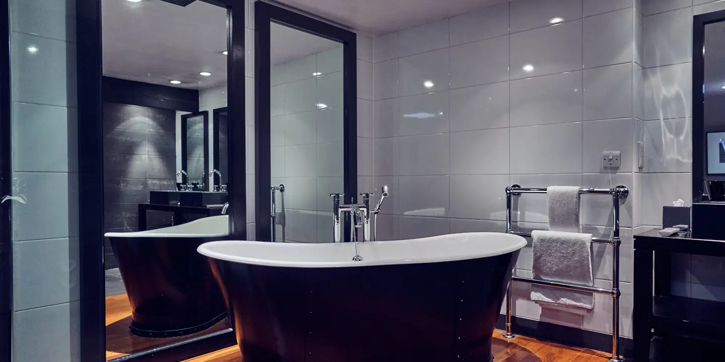 Dark bath tub with heated towel rail on wall.