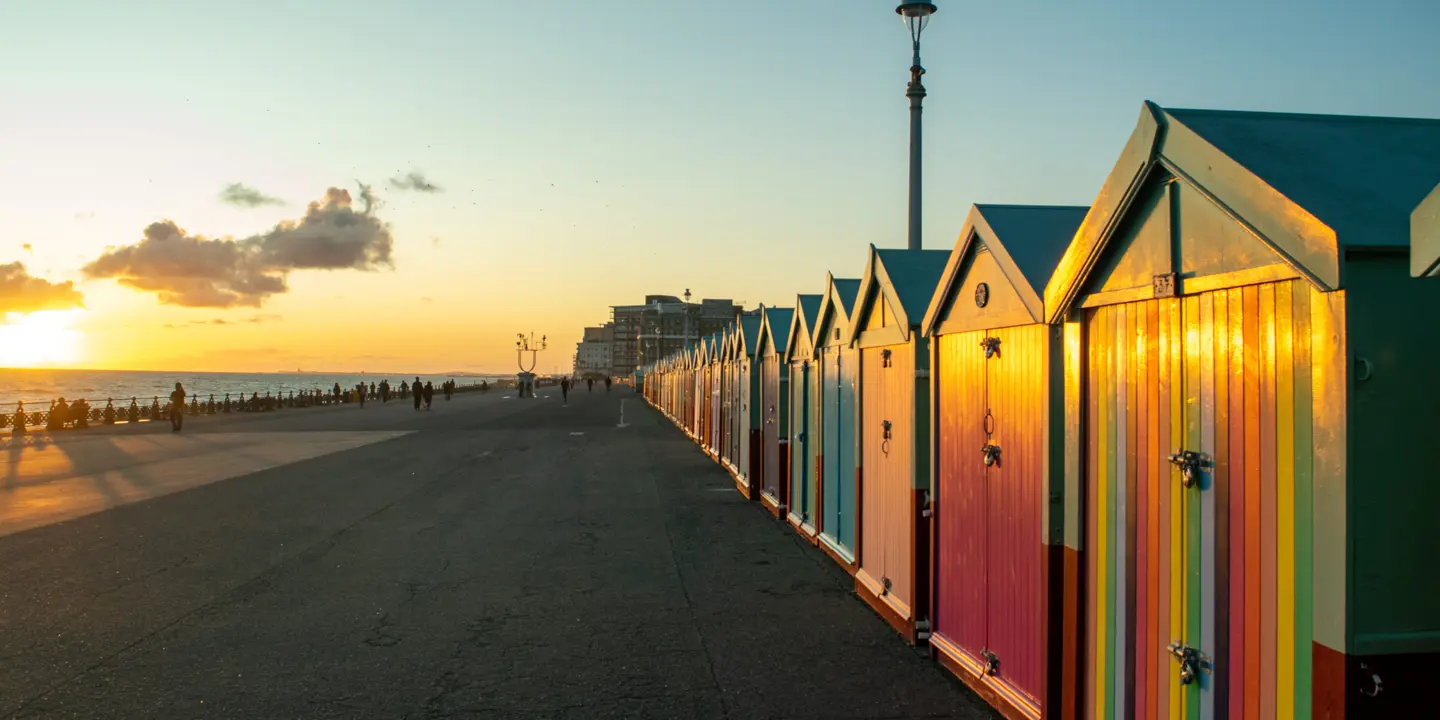 Row of vibrant coloured beach huts along Brighton promenade at sunset.