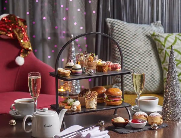 A table displaying a tray of appetizing food accompanied by a glass of fine wine and Christmas decorations in the background.